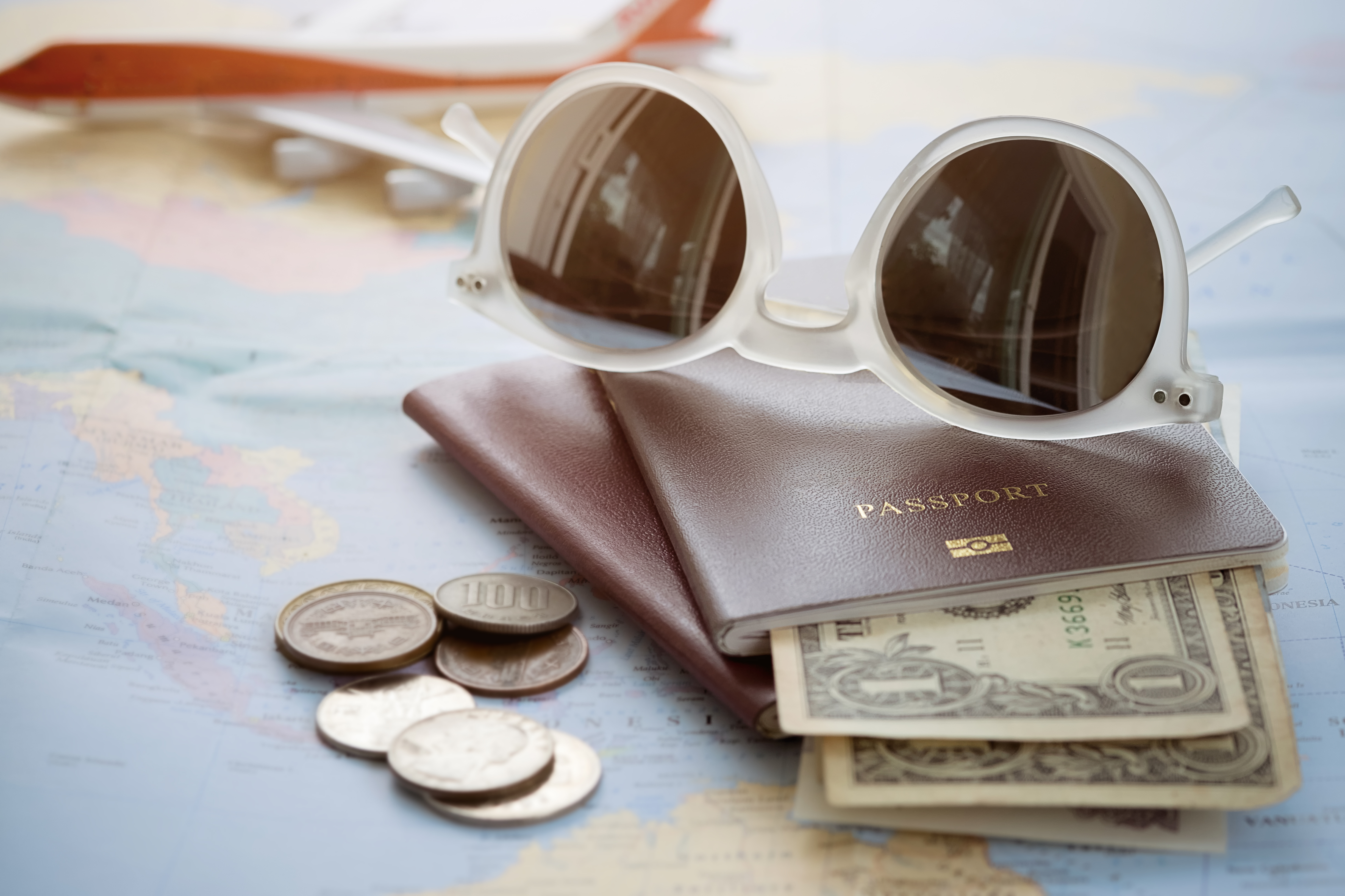 Sunglasses sitting on top of a passport that's holding dollar bills.
